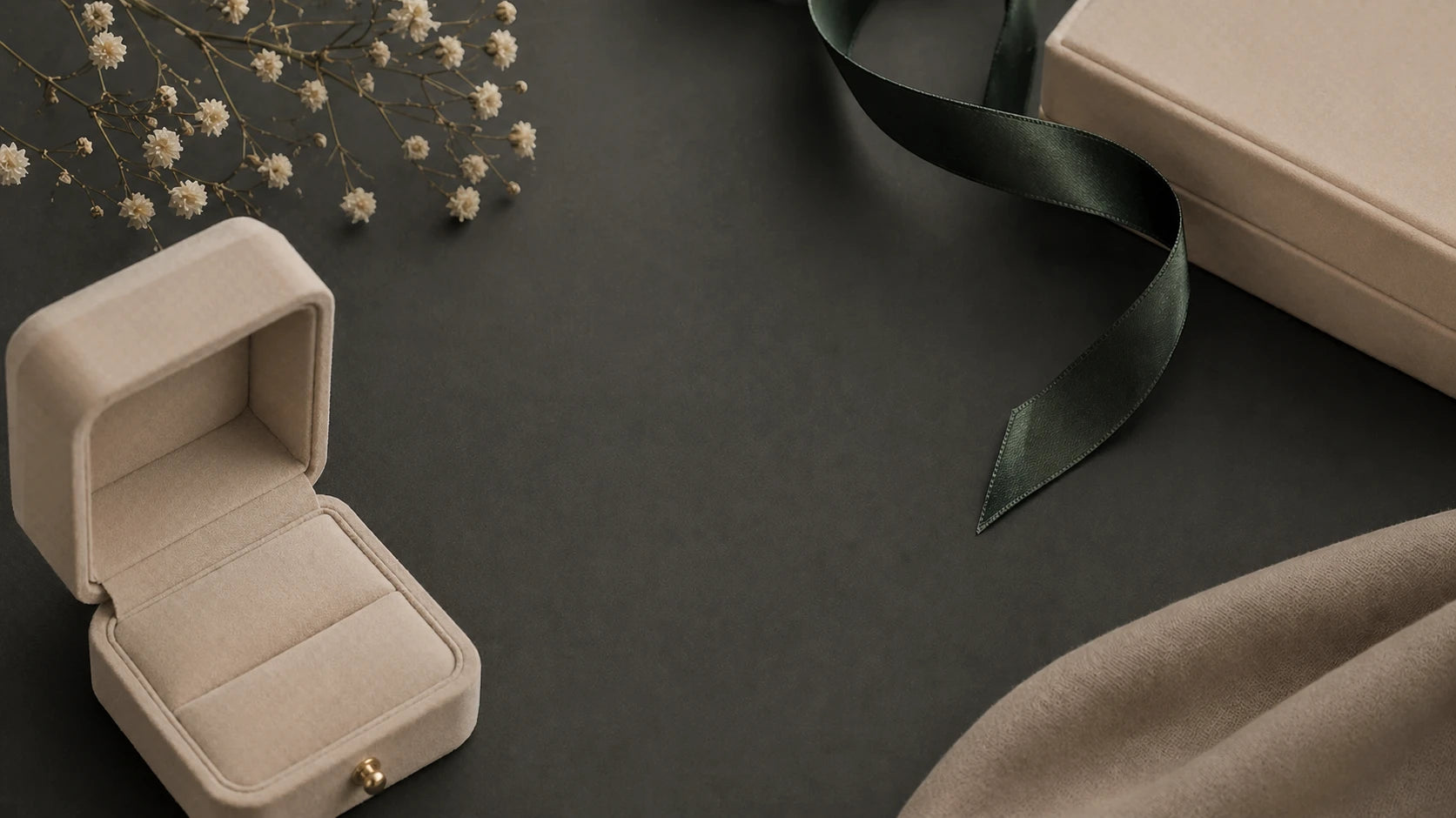Beige jewelry box on a dark surface with a green ribbon and flowers.